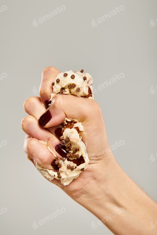 Preview: young unknown female with nail polish squeezing delicious donut with white icing on gray backdrop