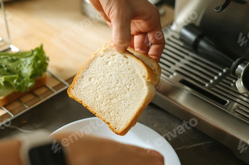 Preview: Hand holding slice of white bread by toaster in kitchen setting