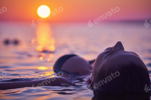 Preview: Silhouette of young woman practicing yoga on the beach at sunrise