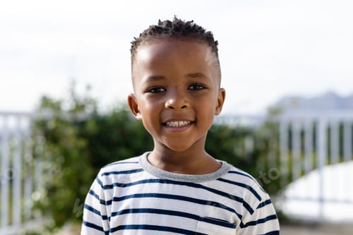 Preview: Portrait of cute african american boy smiling at camera while standing against clear sky in yard