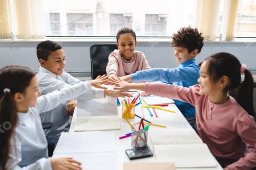 Preview: Diverse small schoolchildren putting hands together at classroom