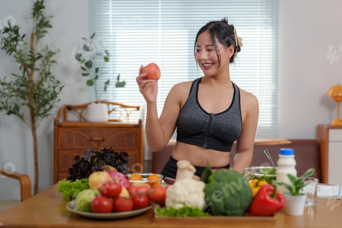 Preview: Young asian woman showing apple with fresh vegetables and fruits on table for a healthy meal at home
