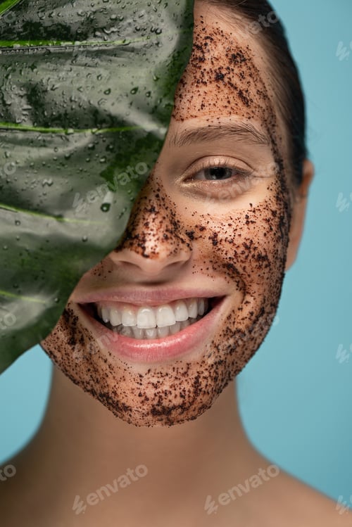 Preview: beautiful happy girl with coffee scrub on face, isolated on blue with leaf