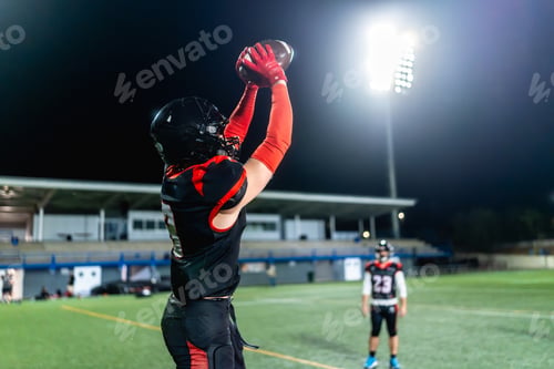 Preview: American football player catching ball during night game