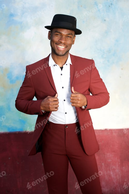 Preview: cool young african american male fashion model smiling with hat and vintage suit by wall