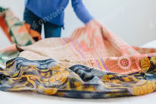 Preview: A woman spreading a fabric quilt over a bed in a bedroom.