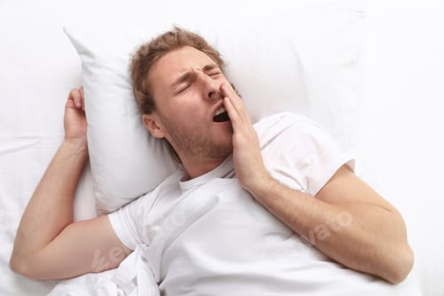 Preview: Handsome young man yawning while lying on pillow in morning, view from above. Bedtime
