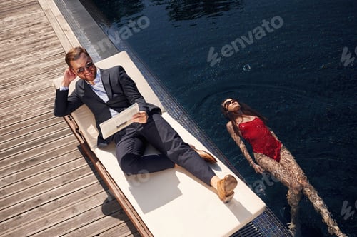 Preview: Business clothes, reading newspaper. Man with woman is in the pool together