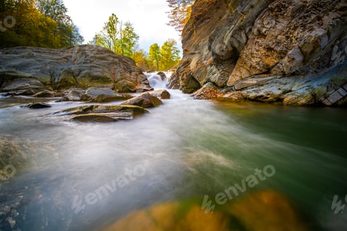 Preview: Mountain river with small waterfall with clear turquoise water falling down between wet boulders