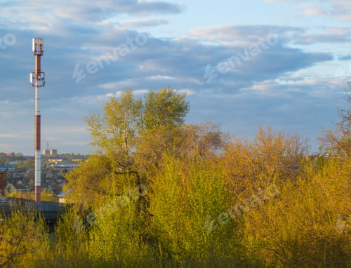 Preview: Cell tower of mobile communication on the background of trees and cloudy sky