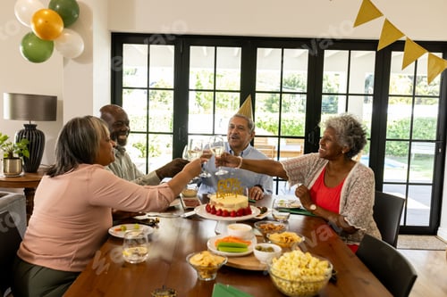 Preview: Toasting with drinks, African American friends celebrating birthday around decorated table