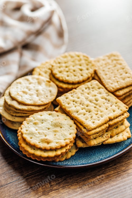 Preview: A stack of crackers neatly arranged on plate on wooden tabletop.
