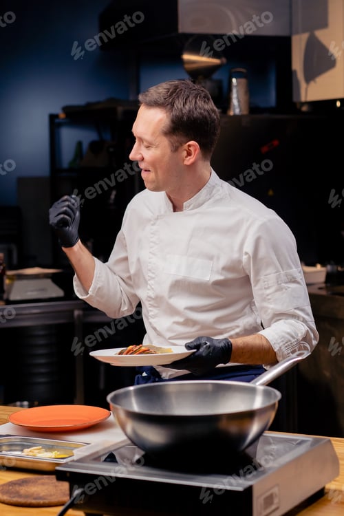 Preview: a chef in a professional kitchen stands a white plate of a ready-made fish dish rejoices and dances