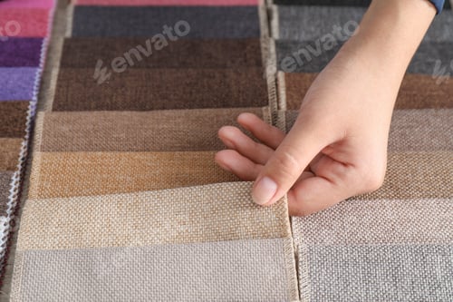 Preview: Young woman choosing among upholstery fabric samples, closeup. Interior design