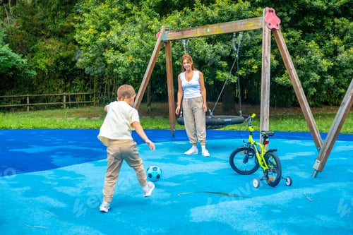 Preview: Child kicking soccer ball with mother at playground on sunny day