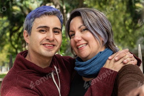Preview: Two smiling friends are hugging and looking at camera. He has blue hair.