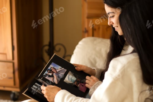 Preview: Beautiful young woman and her mother watching a photo album of themselves