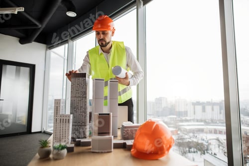 Preview: Engineer man in helmet and reflective vest standing near table with architecture design of city