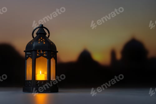 Preview: A black lantern with a candle against a blurred background of a sunset and a mosque.
