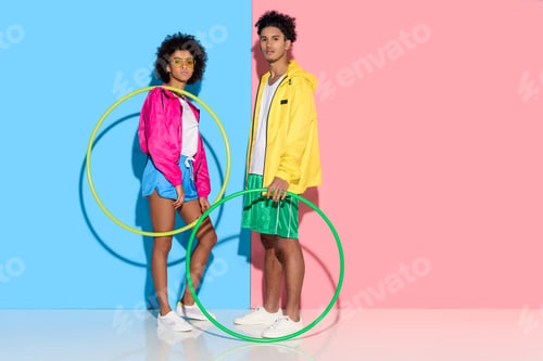 Preview: Young couple standing with hoops and looking to camera on pink and blue background