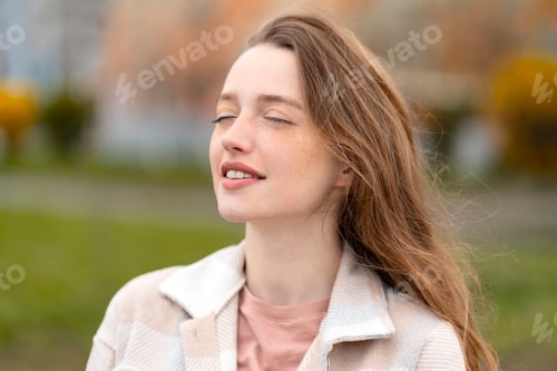 Preview: Cute beautiful woman with closed eyes enjoying sunny day outdoors. Young female on street