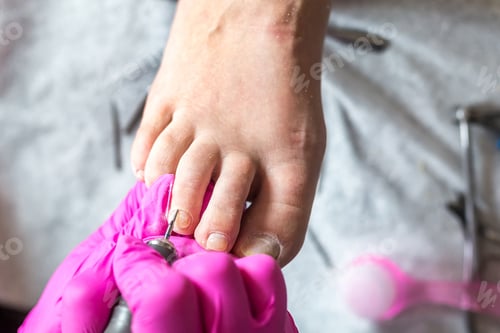 Preview: Pedicurist master in pink gloves cuts the cuticle and shellac toe nails in the pedicure salon