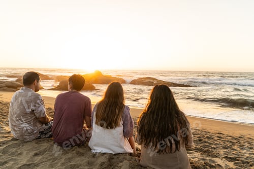 Preview: Group of friends sitting on a beach, gazing at the sea