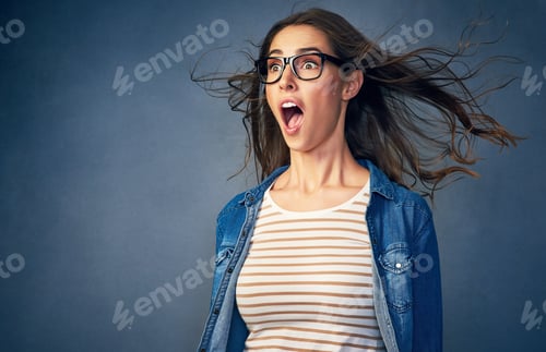 Preview: Surprise. Shot of a happy young woman with air being blown in her face in studio.