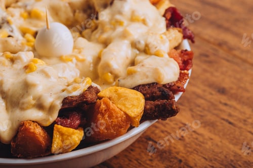 Preview: Closeup shot of a dish with french fries, sausages topped with cheese and corn on a wooden table.