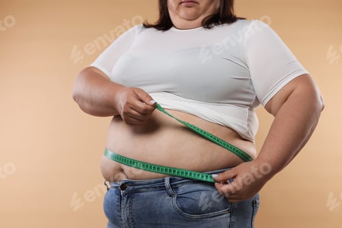 Preview: Overweight woman measuring her belly with tape on beige background, closeup