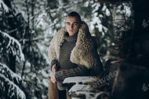 Preview: Ancient viking warrior with steel axe posing near wooden hut in scandinavian forest