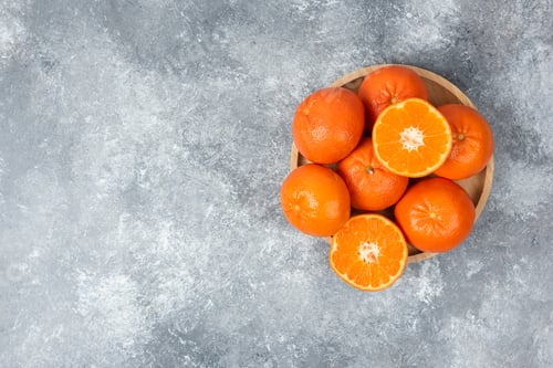 Preview: Juicy orange fruits with slices in a wooden plate on stone background