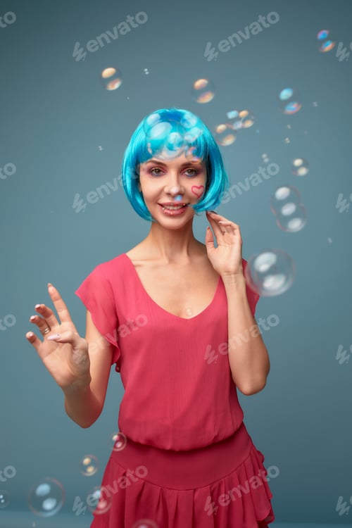 Preview: Beautiful young woman with blue wig and bright make-up in soap bubbles. Fashion model girl with