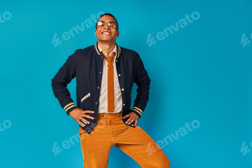 Preview: carefree and stylish african american student with radiant smile looking at camera on blue