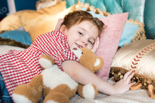 Preview: adorable kid lying with teddy bear and smiling at camera