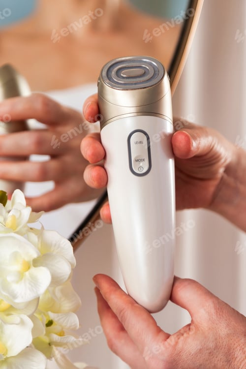 Preview: Hands Gently Hold an Anti-Aging Facial Massager in a Serene Indoor Setting With Elegance