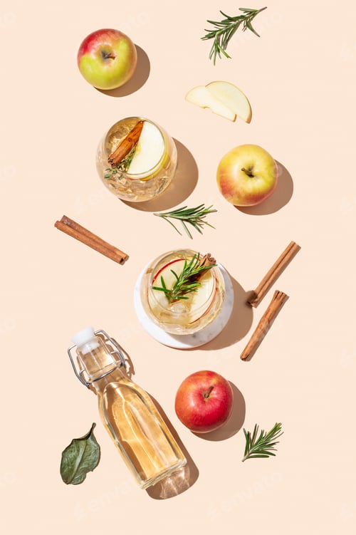 Preview: Flat lay of apple cocktail or cider in a glass with ice, cinnamon and rosemary, bottle and fruits