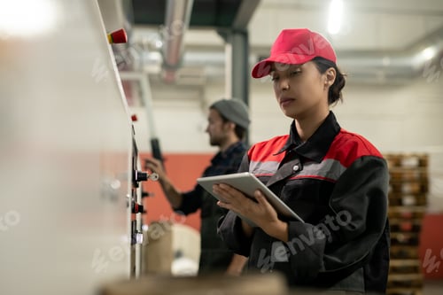 Preview: Young pretty female engineer with tablet entering data from control panel