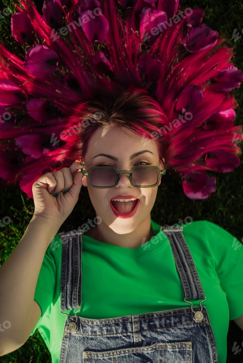 Preview: Portrait of real smiling woman with vivid dyed pink fuchsia hairstyle lying on green lawn