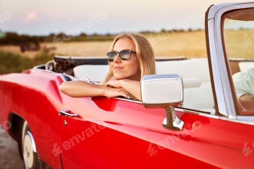Preview: Beautiful woman sitting in car at sunset