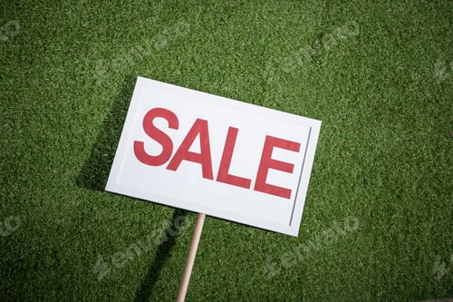 Preview: white sale banner lying on green grass, house for sale concept