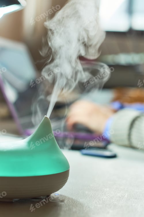 Preview: Woman uses aroma diffuser while working. Aromatherapy concept.