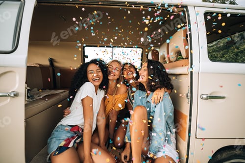 Preview: Group of happy women sitting in a camper van door under confetti. Friends having fun on a road trip.