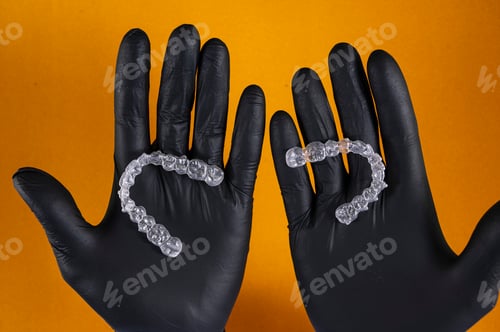 Preview: Doctor hand holding a clear dental aligner with the yellow background