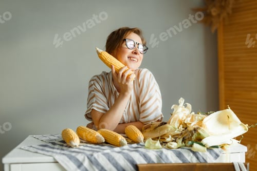 Preview: Young pretty girl on a gray background holding corn cobs in her hands