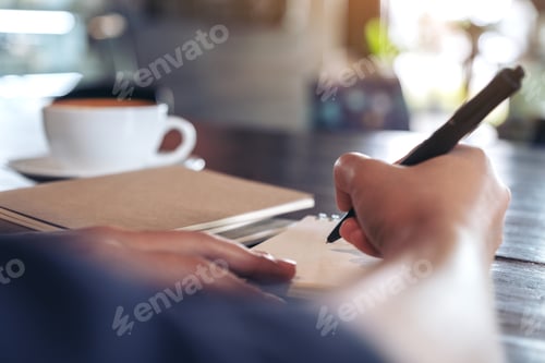Preview: Closeup image of a woman writing on blank notebook on table in cafe