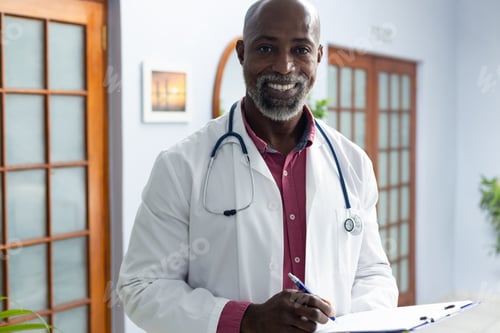 Preview: Portrait of happy african american male doctor holding clipboard and smiling at doctor's office