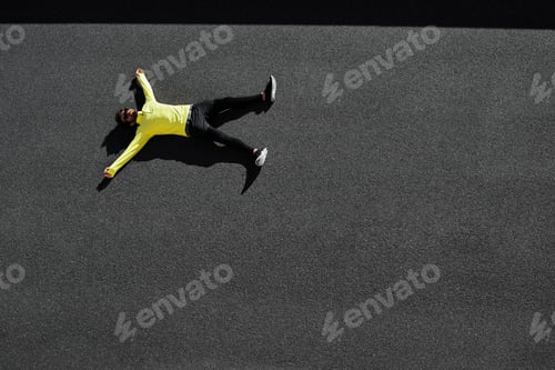 Vista previa: Top view runner in yellow sportswear resting lying on a black asphalt after running. Jogging man tak
