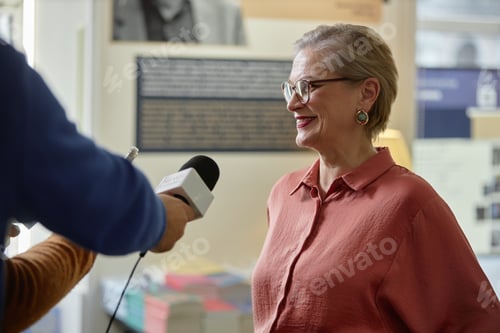 Preview: Caucasian Senior Woman Smiling While Giving Interview to Journalist Indoors