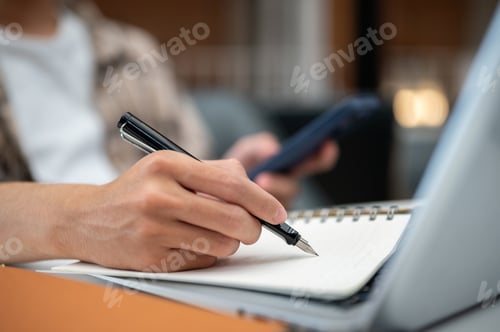 Preview: Close up of a man hands holding phone and writing in notebook with a pen over sits at table in cafe.